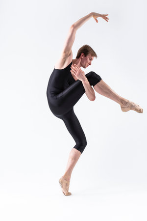 Ballet Dancer Man in Black Dance Suit Tights Posing in Ballanced Dance Pose While Stretching His Arm and Leg Muscles in Studio on White. Vertical Compositionの写真素材
