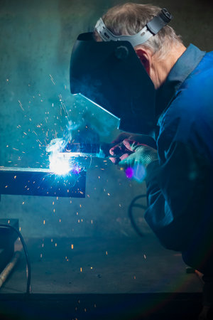 Male Welder in Protective Mask During Welding Process of Metal Rod At Workshop. Vertical image...