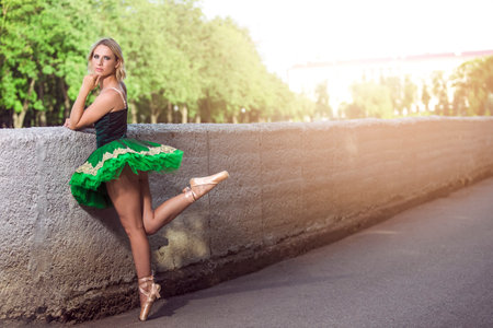 Relaxed Professional Caucasian Ballet Dancer in Green Tutu Dress Posing in Standing Position With Lifted And Stretched Leg On Sunny Sky Outdoors. Horizontal imageの写真素材