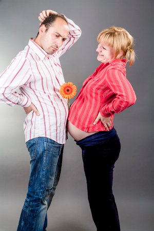 Young Embarrassed Caucasian Couple Expecting Baby Standing Together Indoors While Holding Flower Between Them.Vertical Compositionの写真素材