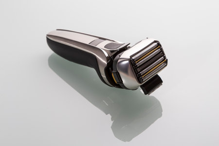 Upper Close Up View of Black Modern Stylish Electric Mens Washable Shaver With Separated Blades Unit on White Reflective Surface. Horizontal Shotの写真素材