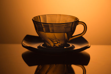 One Set of Glass Teacup Filled With Water and Plate isolated Over Glowing Orange Gradient Background. Horizontal imageの写真素材