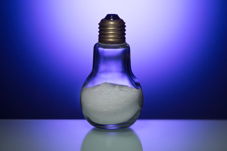 Image of Glass Bulb Lamp Filled with Salt Powder Over Glowing Blue Background. Horizontal Image...