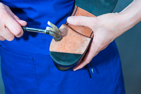 One Professional Shoemaker in Apron Repairing Sole of Black Polished Leather Mens Shoes With Hammer in Workshop. Horizontal Image Orientationの写真素材