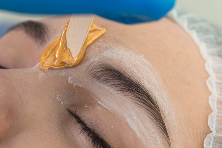Eye of Caucasain Female During Eyebrow Epilation At Facial Depilation Using Wood Sticks and Flowing Wax During Professional Eyebrow Permanent Makeup in Salon. Horizontal Compositionの写真素材