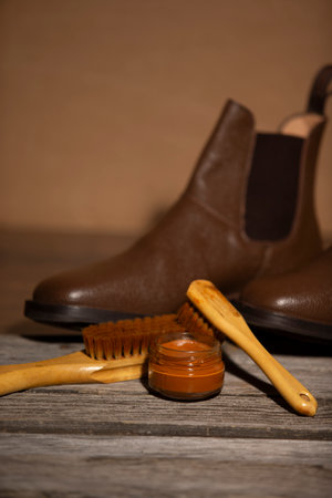 Lineup of Various Traditional Shoes Cleaning Accessories for Dark Brown Shagreen Grain Leather Chealsey Boots Made of Calf Leather with Special Tools On Wooden Background With Focus on Wax Creamの写真素材