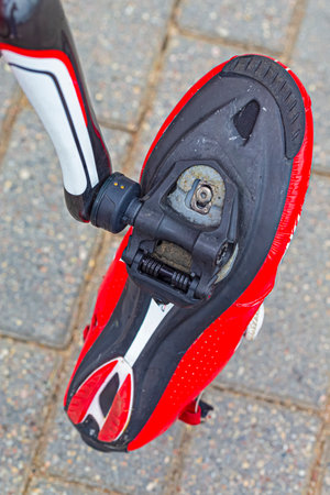 Sport Concept. Red Dirty Cycling Professional Carbon Shoes with Cleats Hanged On Road Bike Pedals At...