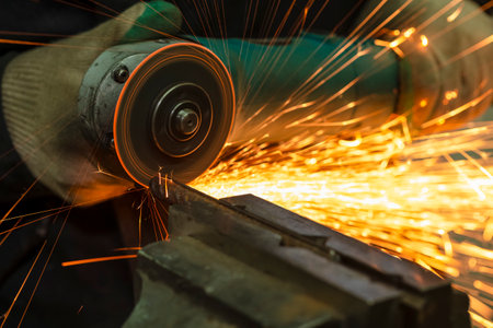 Hands of Male Fitter in Protective Gloves and Uniform With Gringer Tool For Metal Work With Bunch of Sparks in Workshop. Horizontal Imageの写真素材