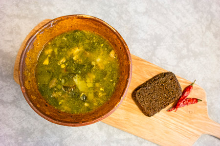 Upper View of Ceramic Bowl of Classical Sorrel Soup With Chicken Meat and Vegetables With Loafs of Fresh White Bread And Red Pepper Over Rustic Wooden Background. Horizontal Image Compositionの写真素材