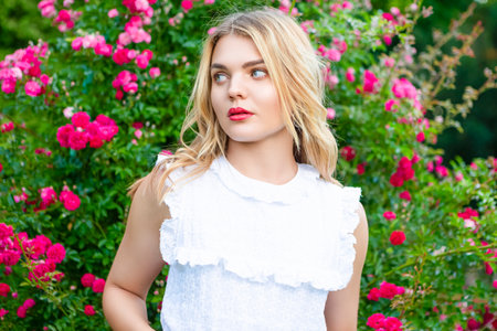 Winsome Beautiful Girl in Spring Garden Near Blossoming Flowering Bush in Fashion White Dress in Park Near Flowers Blossom Resting in Aromatic Nature. Horizontal Image Orientationの写真素材