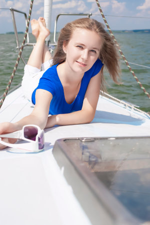 Winsome Happy and Smiling Positive Caucasian Sailor Woman Laying On Deck Relaxing on White Yacht At Daytime on Board. Vertical imageの写真素材