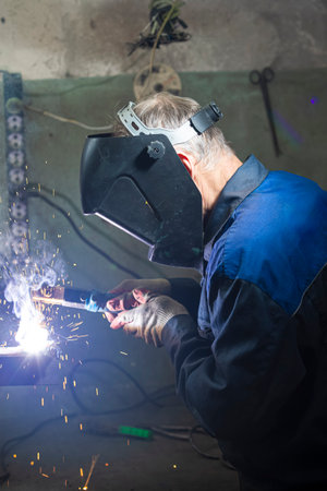 Working Professional Male Welder in Protective Mask During Welding Process of Metal Rod At Workshop....