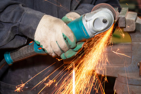 Closeup of Hands of Male Fitter in Protective Gloves and Uniform With Gringer Tool For Metal Work With Bunch of Sparks in Workshop. Horizontal Compositionの写真素材
