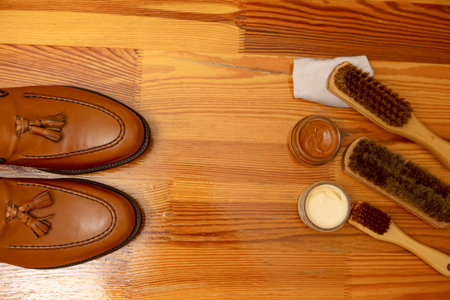 Pair of Tan Tassel Loafers Shoes Made of Calf Leather with Leather Sole Placed In Line With Shoe Cleaning Brushes On Wooden Background. Horizontal Shotの写真素材