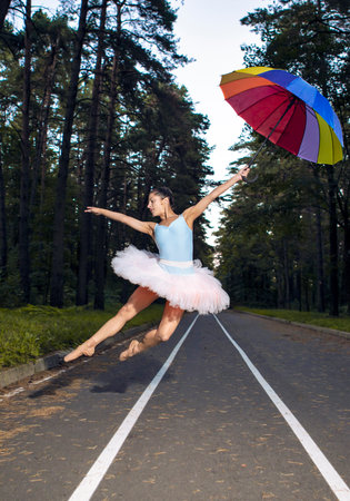 Caucasian Ballet Dancer in Rose Pink Tutu Posing With Colorful Umbrella During Ballet Pas in Summer Forest Outdoor. Vertical Orientationの写真素材