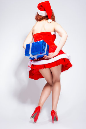 Christmas and New Year Ideas. Back and Legs of Caucasian Santa Helper with Christmas Presents Behind Wrapped Gift in Hands. Vertical Shotの写真素材