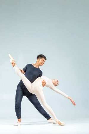 Flexible Couple of Asian Man and Caucasian Woman Performing As Ballet Dancers Over Grey in Studio As Classical Choreography and Ballet Dancing. Vertical Image Orientationの写真素材