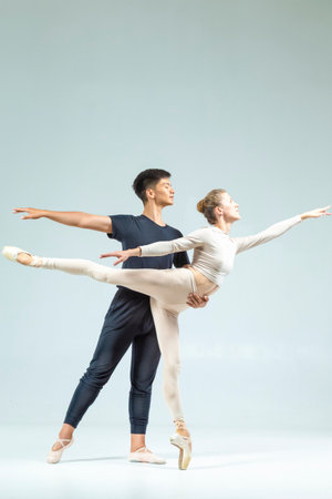 One Loving Couple of Asian Man and Caucasian Woman Performing As Ballet Dancers Over Grey in Studio...