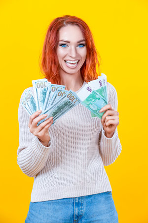 Cheerful Young Winsome Woman Holding Stack of Money Banknotes and Celebrating Isolated Over Yellow Background. Vertical Compositionの写真素材