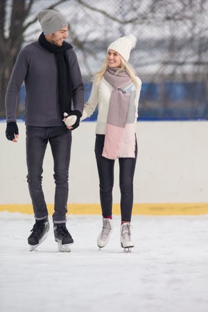 Smiling Happy Positive Caucasian Couple Ice Skating Together on Skating Rink And Having Good Time Together Holding Hands. Vertical image Orientationの写真素材