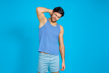Handsome Brunet Man in Striped Underware During Early Morning Yawing While Scratching His Head From Behind Against Seamless Blue Background. Horizontal Image Compositionの写真素材