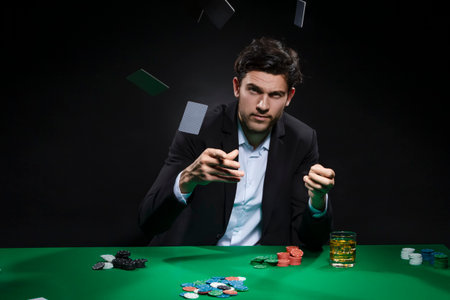 Risky Caucasian Young Handsome Pocker Player Throwing Cards Staking and Betting To Win At Pocker Table With Chips And Cards to Depict Casino and Gambling Concepts. Horizontal Imageの写真素材