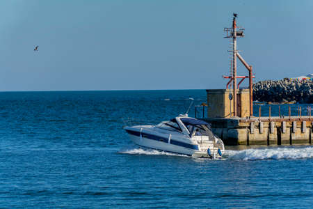 Luxury yacht leaving port of Tomis, Constanta. White cabin cruiser over blue water. Luxury motor boat in navigationの写真素材