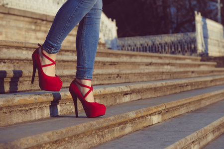 Woman wearing blue jeans and red high heel shoes in old town. The women wear high heels walk down stairs. Sexy legs in red high heel shoes. Trendy fashion lookの写真素材