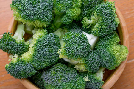 overhead table top view fresh organic broccoli in wood bowl over kitchen table,の写真素材