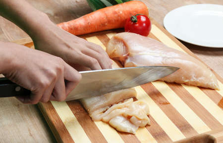 a young woman's hand cutting chicken to prepared dinnerの写真素材