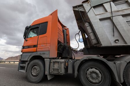 orange truck moves dirty dark industrial container in a dark overcast settingの写真素材