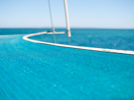 bow of a yacht boat with a green sea and blue sky backdrop and tight safety material