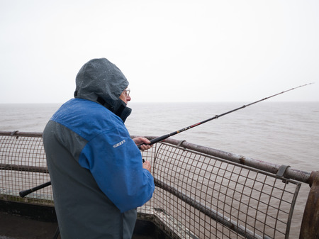 England, Blackpool, 04/22/2015, Fisherman fishing off a blackpool pier into the dirty cold gloomy north sea.のeditorial素材