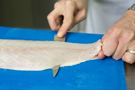 Filleting and removing the bone from a fresh fish on a blue cutting board using a sharp knife.