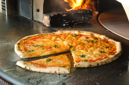 Gourmet Margherita pizza fresh from the pizza oven, with wood flame in the backgroundの写真素材