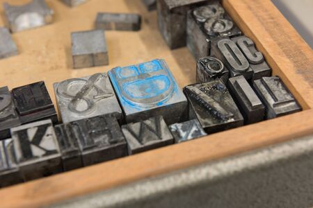 Vintage lead letterpress printing blocks against a weathered wooden drawer background with bokeh.の写真素材