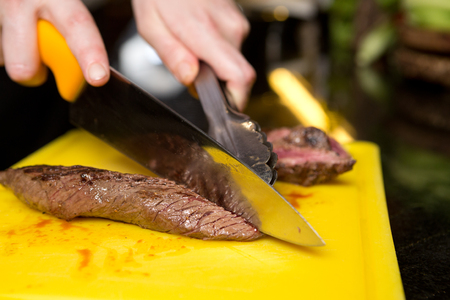 Cutting flame grilled, cooked kangaroo steak loin on a yellow cutting boardの写真素材