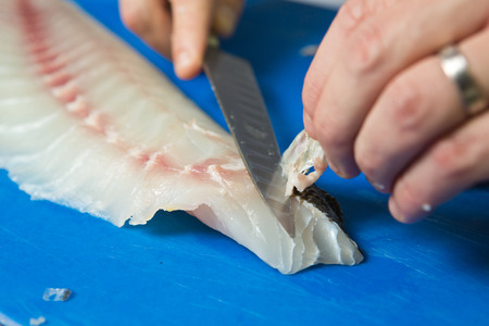 Filleting and removing the bone from a fresh fish on a blue cutting board using a sharp knife.の写真素材