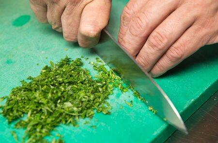 Organic fresh parsley being finely chopped on a green cutting board.の写真素材