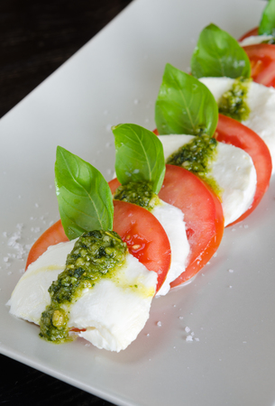 Caprese Salad,Vine ripeTomato and Mozzarella slices with basil leaves and fresh green pesto.の写真素材