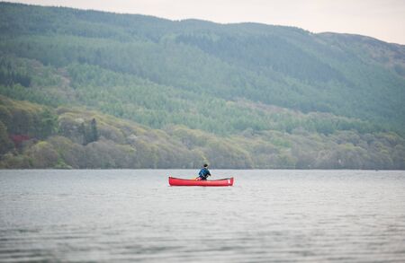 Lake Coniston, England, 06/06/2016, A lonely canoeist  on lake coniston, The Lake District, with a foggy green forest backdrop.のeditorial素材