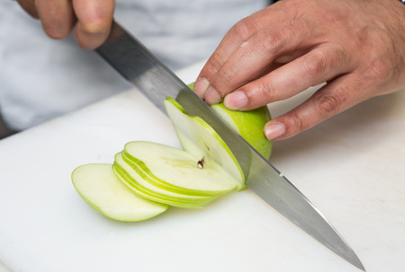 A knife slicing thin slices of fresh organic green apple, on a white cutting board.の写真素材