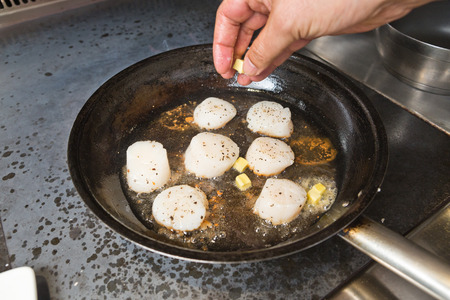 Delicious pan seared organic scallops being seared in melted butter, in a metal cooking pan on the hob. Presented professionally and shot with a shallow depth of field.の写真素材