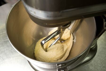 Thick creamy pastry dough. being mixed in a metal bowl by an industrial mixing machine, with a soft depth of field.の写真素材