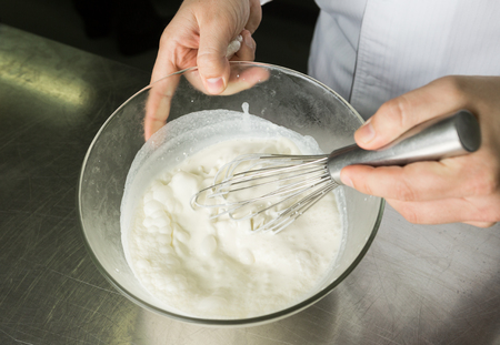 A beautiful rich and creamy , white whipped cream mixture, being hand whisked in a large glass mixing bowl.の写真素材