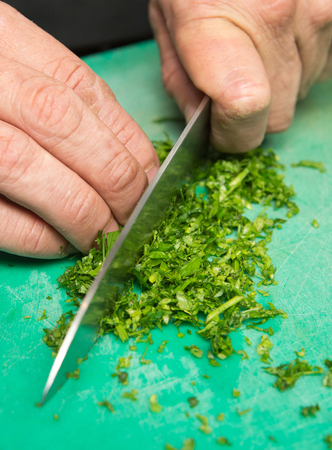 Organic fresh parsley being finely chopped on a green cutting board.の写真素材