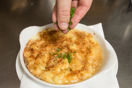 Chopped fresh parsley being sprinkled onto oven baked macaroni cheese.の写真素材