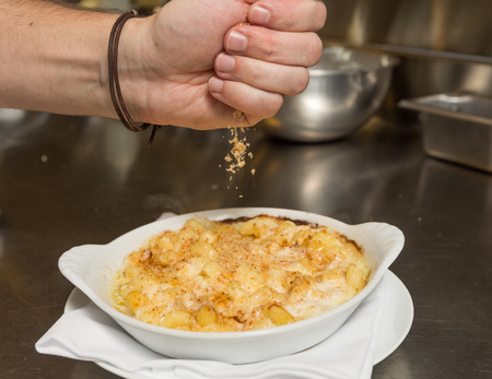 Cooked breadcrumbs being sprinkled onto oven bake macaroni cheese.の写真素材