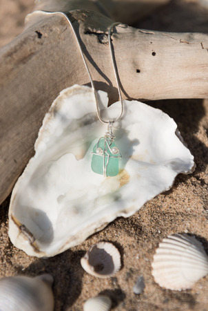 Unique handmade aqua marine blue sea glass jewellery, with a silver chain on a rustic sand and seashell backgroundの写真素材