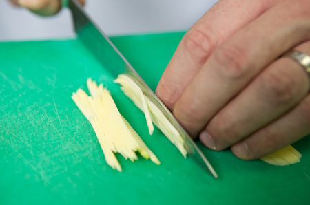 A fresh young green organic mango, being hand sliced into thins slices on a green cutting board